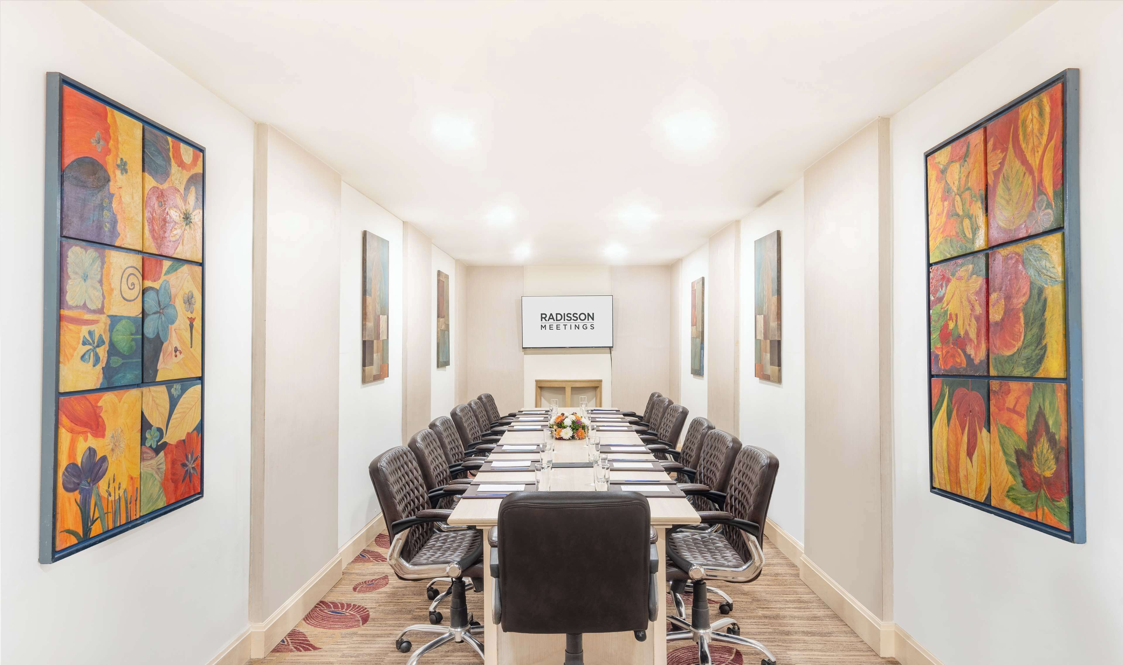 Ein Konferenzraum mit einem langen Tisch, Stühlen und großen floralen Gemälden an den Wänden.