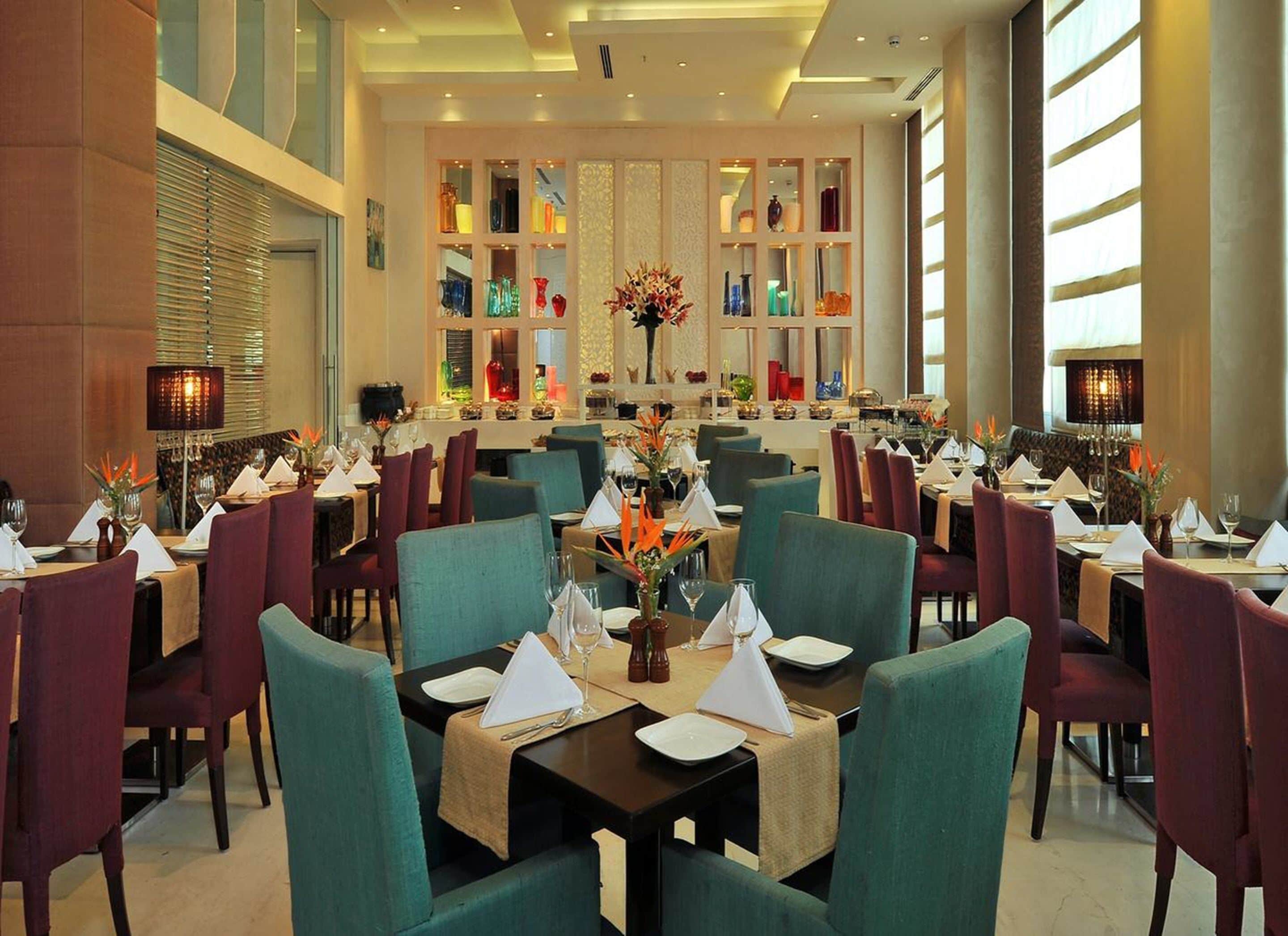 A spacious dining area with multiple tables and chairs, a central decorative vase, and a wall of colorful glass vases.