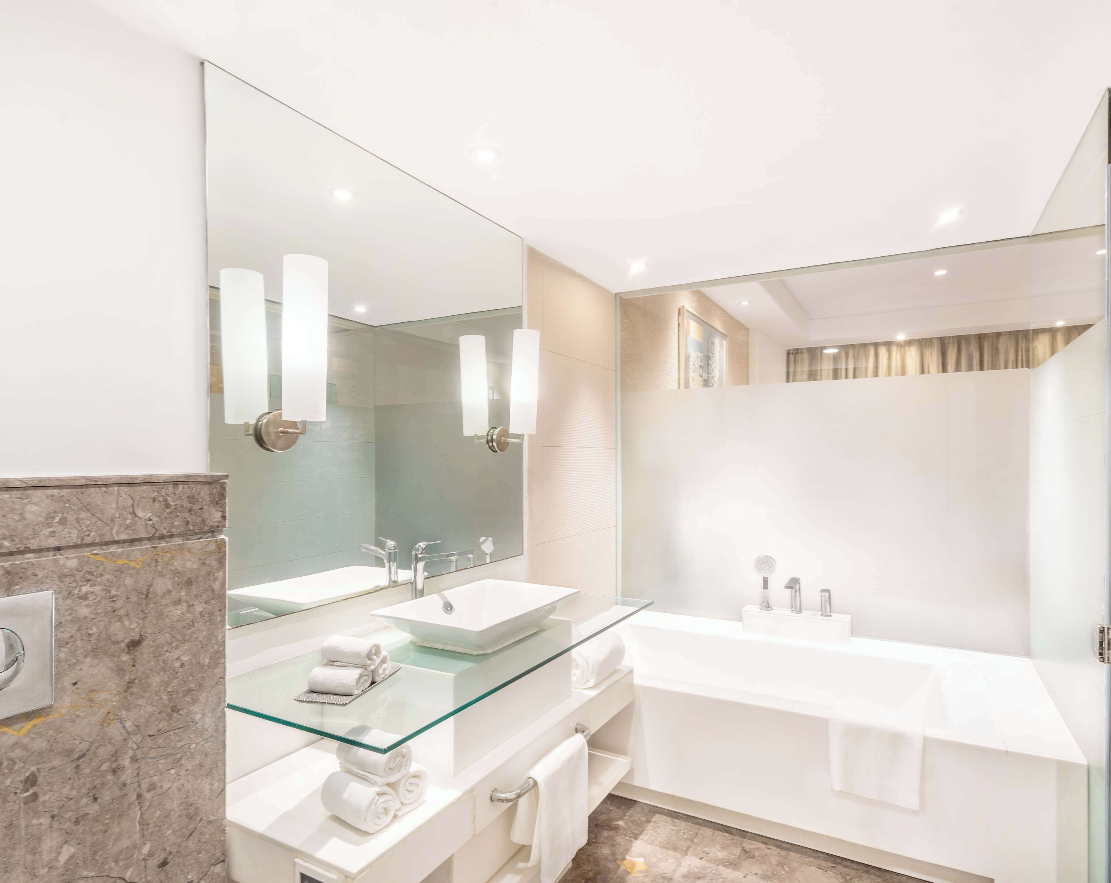 Une salle de bain moderne avec deux vasques, un meuble-lavabo surmonté d’une plaque de verre et un grand miroir.