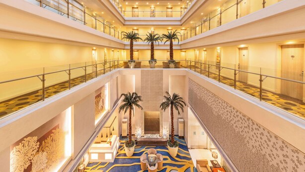 Un hall d’hôtel à plusieurs niveaux, doté d’un atrium central, de rampes en verre et d’un tapis à motifs.