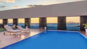 Un espace piscine aménagé sur le toit, avec des chaises longues et une vue sur le panorama urbain.