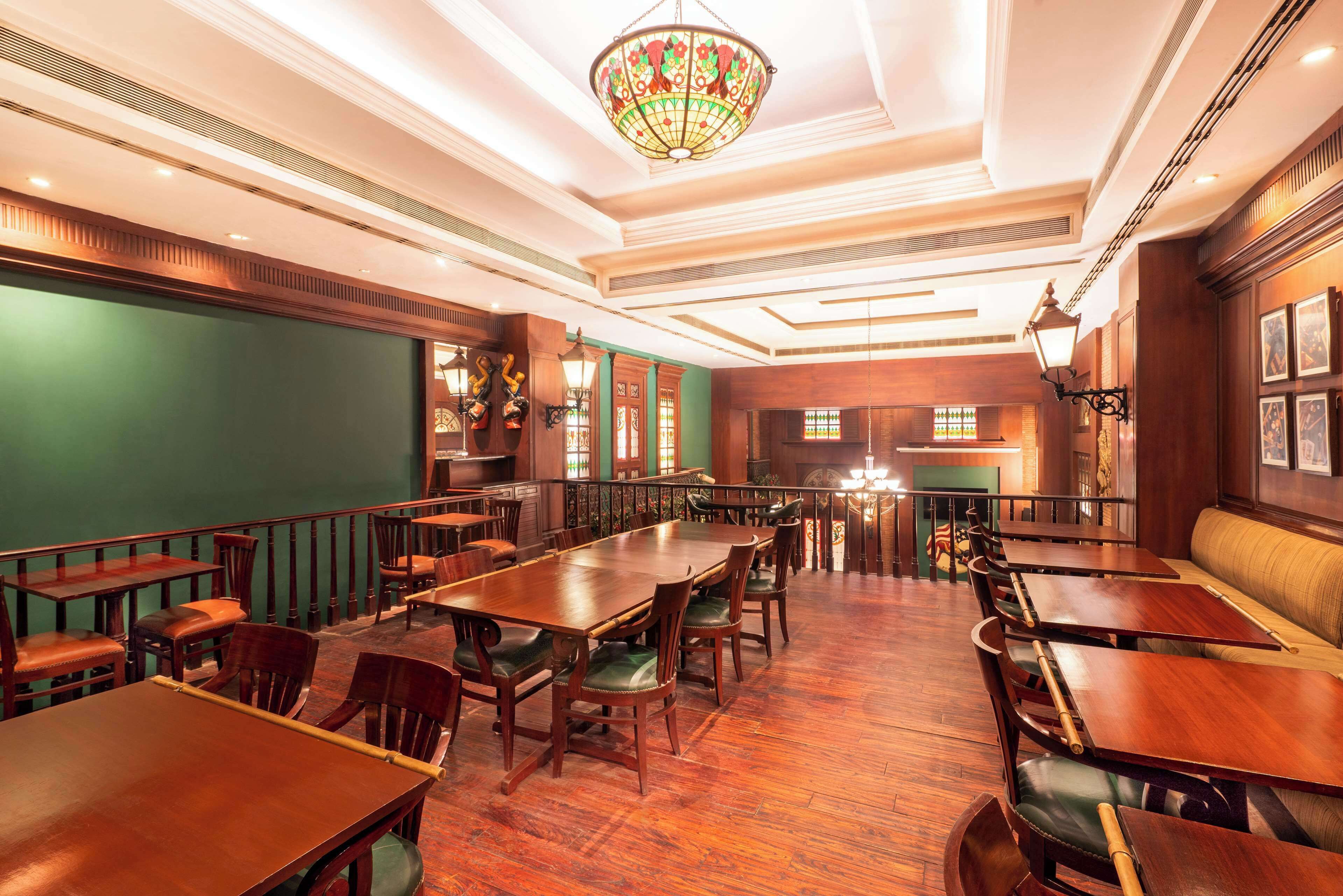A spacious restaurant with wooden tables and chairs, a green wall, and a decorative chandelier.