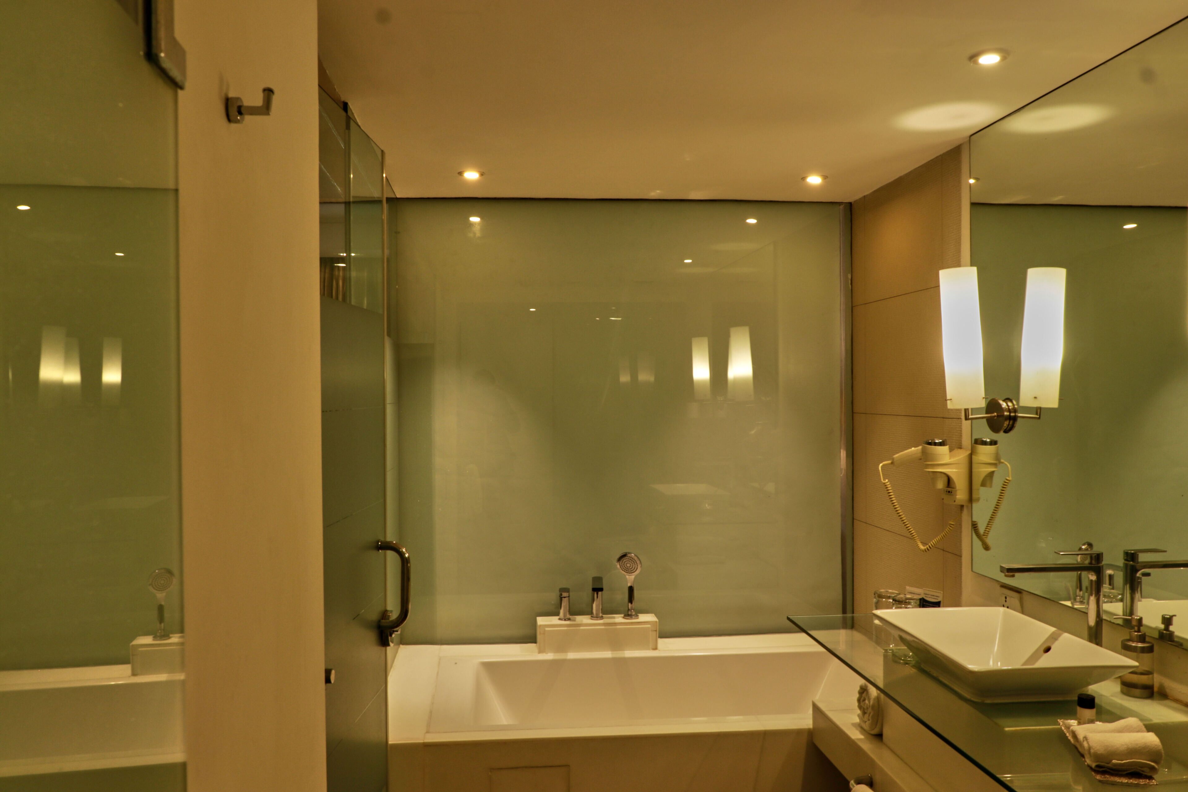 A modern bathroom with a glass-enclosed shower, a white bathtub, and a large mirror with wall-mounted lights.