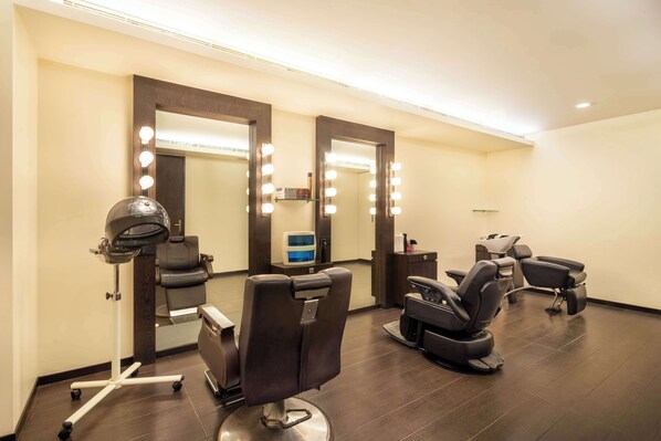 Un salón de belleza con dos sillones de peluquería, un secador de pelo sobre un soporte y un espejo con iluminación.