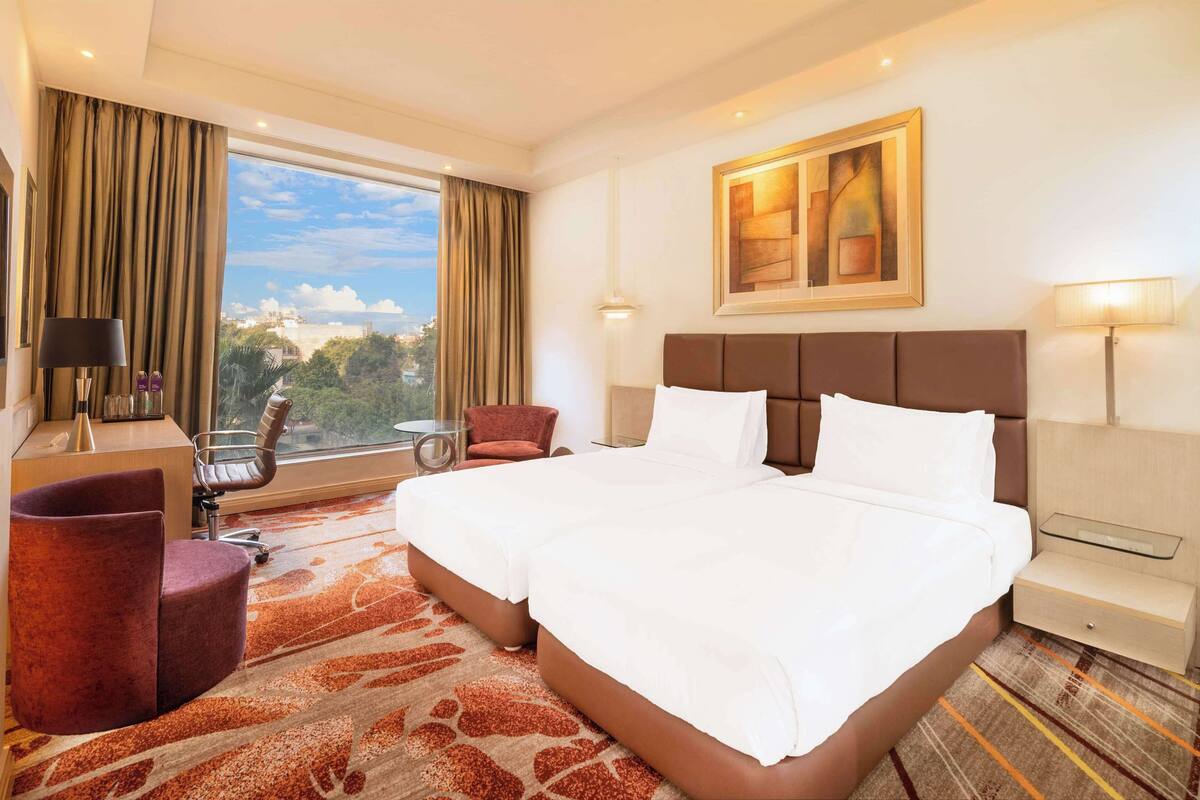 Habitación de hotel con una cama grande, un escritorio con lámpara, una silla y vistas a la ciudad.