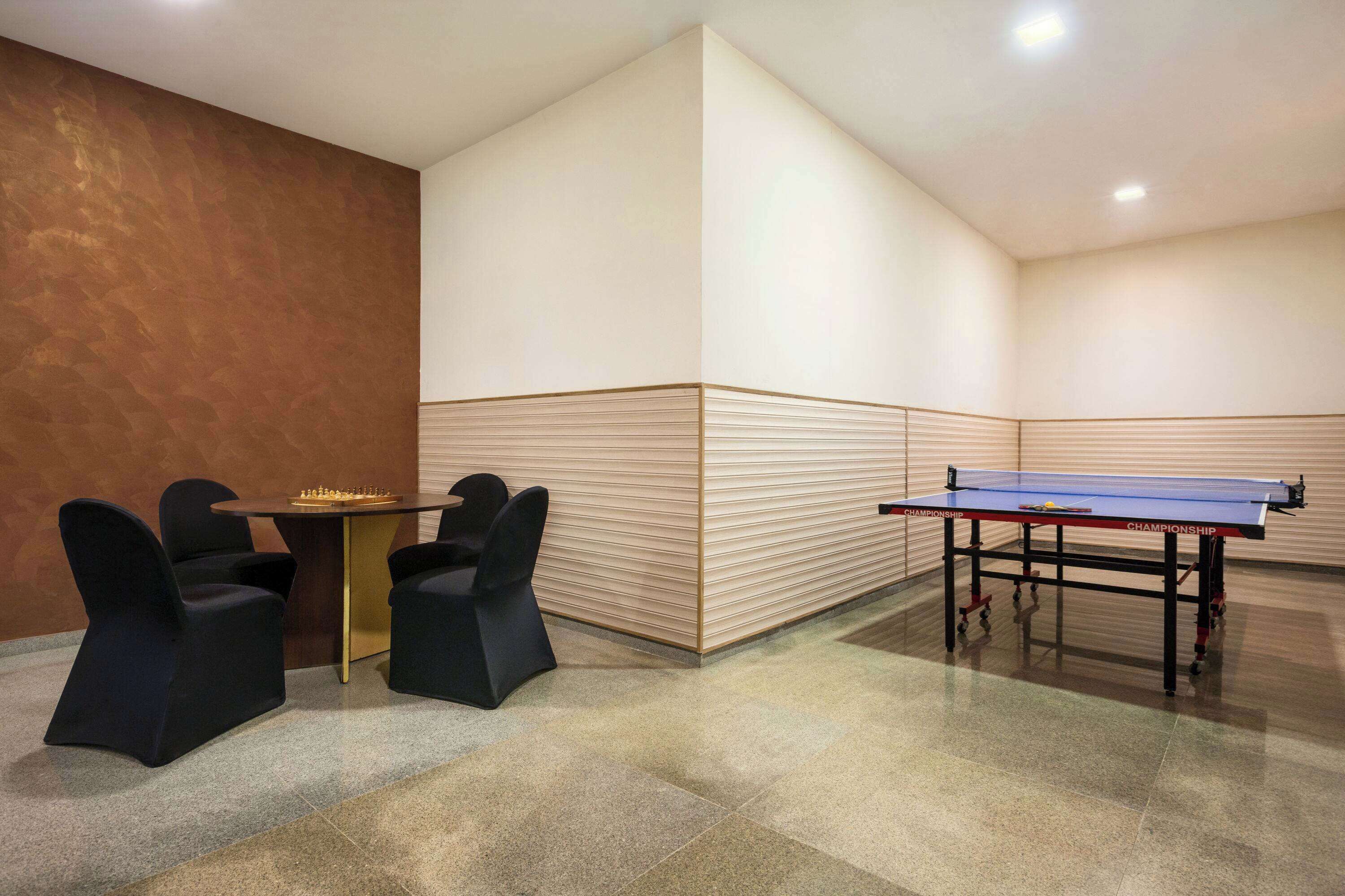 A ping pong table with chairs and a small table with a chess set in a room with a tiled floor and a wooden accent wall.