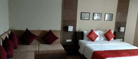 A hotel room with a bed, a sofa, and a small table. There are two wall-mounted lamps and a picture frame on the wall.