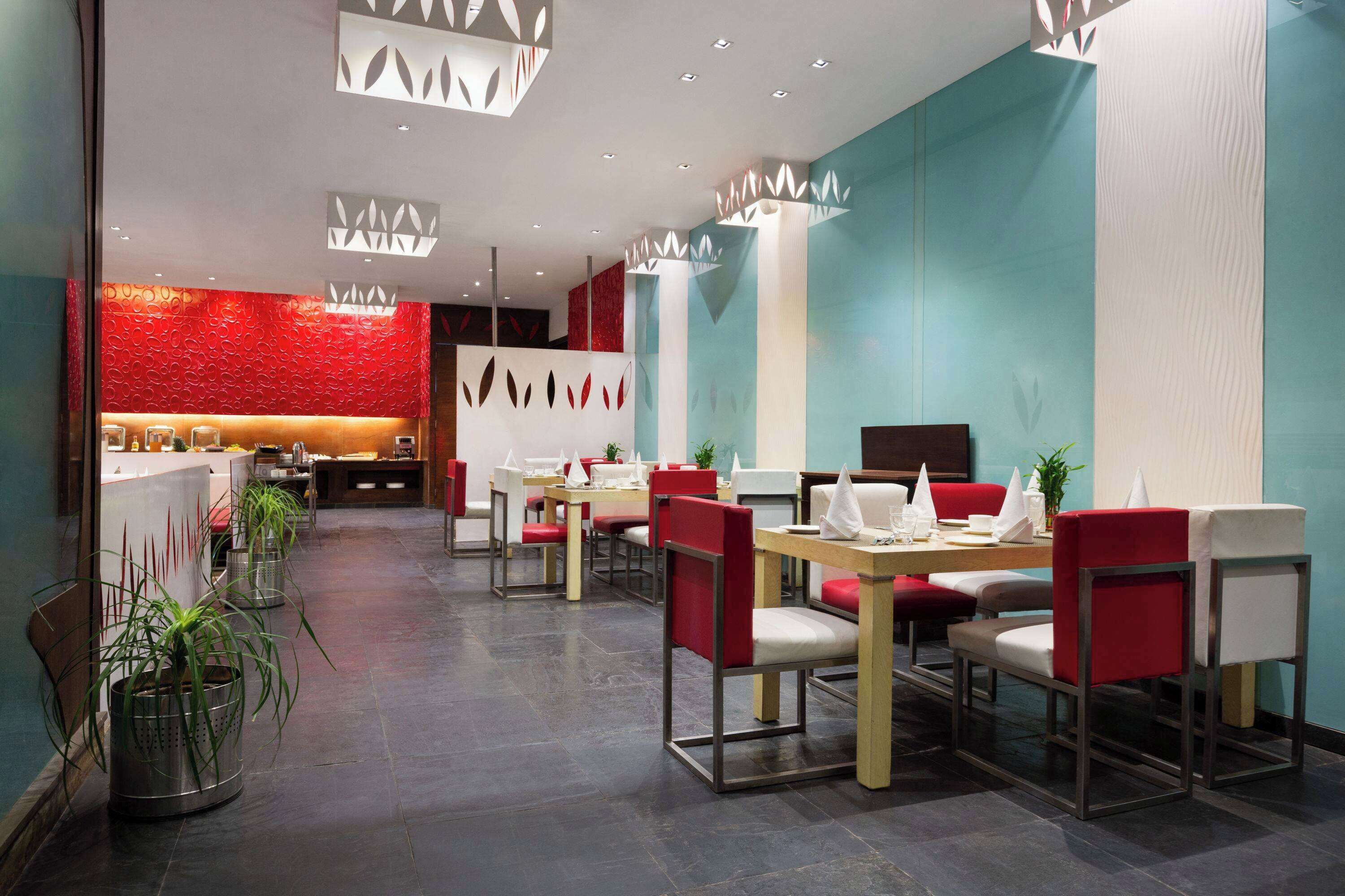 Un restaurante moderno con decoración en rojo y blanco, varias mesas de comedor y plantas en macetas.