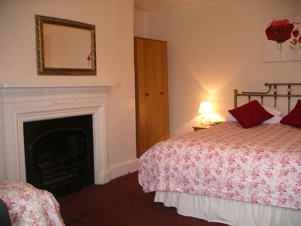 Un dormitorio con chimenea, una cama con almohadillas rojas, una mesita de noche con lámpara y un armario de madera.