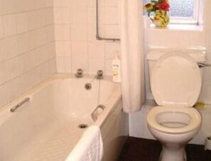 A bathroom with a bathtub, toilet, and a window with flowers. - OYO La Spada Boutique Hotel  (Durham)