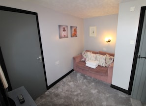 A small, cozy room with a grey door, a pink sofa with floral cushions, and two framed pictures on the wall. - The Lorna Doone Hotel (Minehead)