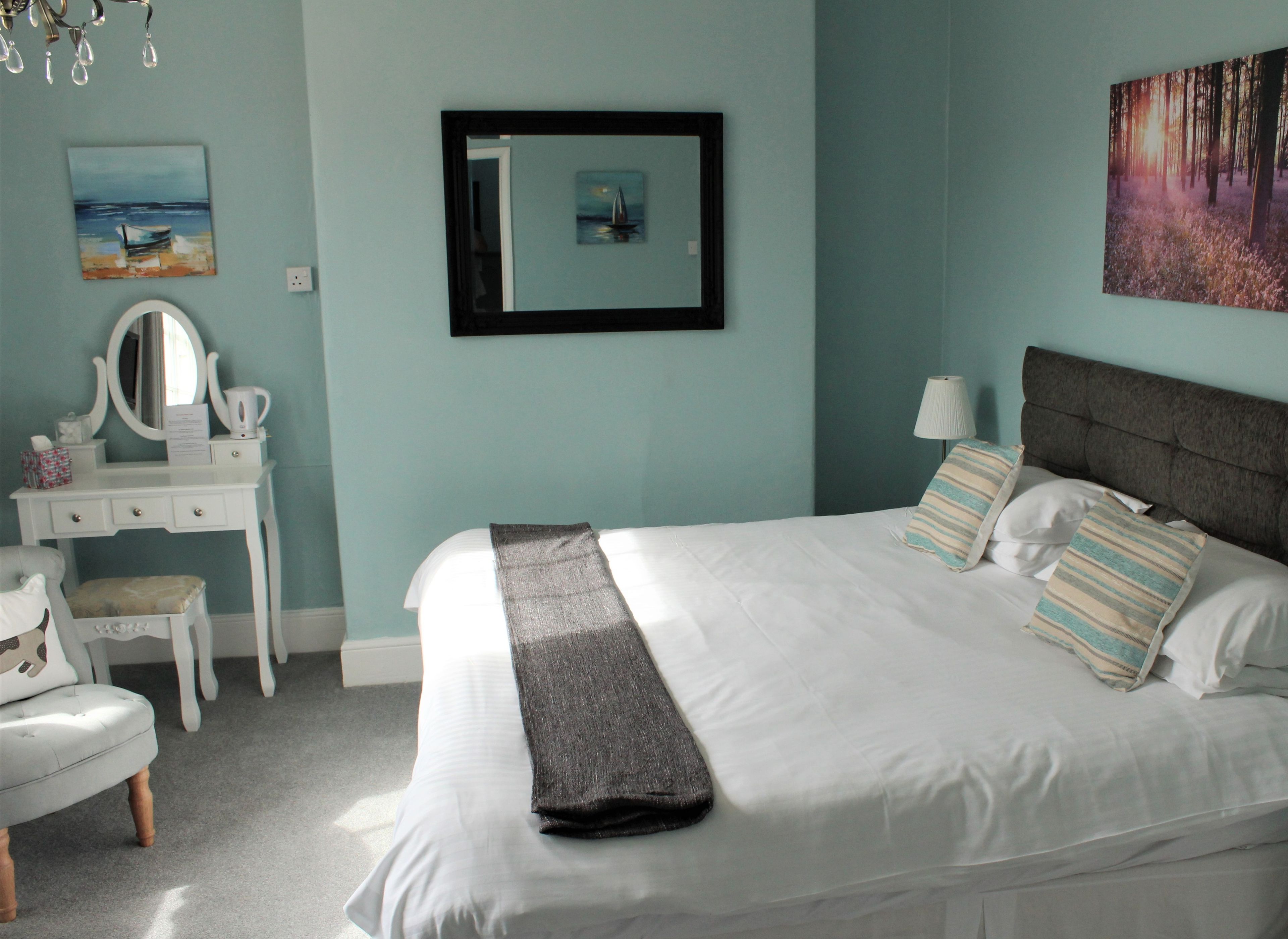 Un dormitorio con cama, cómoda, silla, espejo y obras de arte en las paredes.