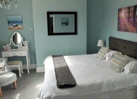 Un dormitorio con cama, cómoda, silla, espejo y obras de arte en las paredes.