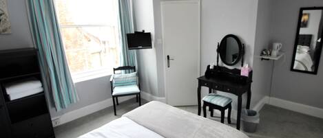 A bedroom with a bed, a vanity with a mirror, a chair, a dresser, and a window with curtains.