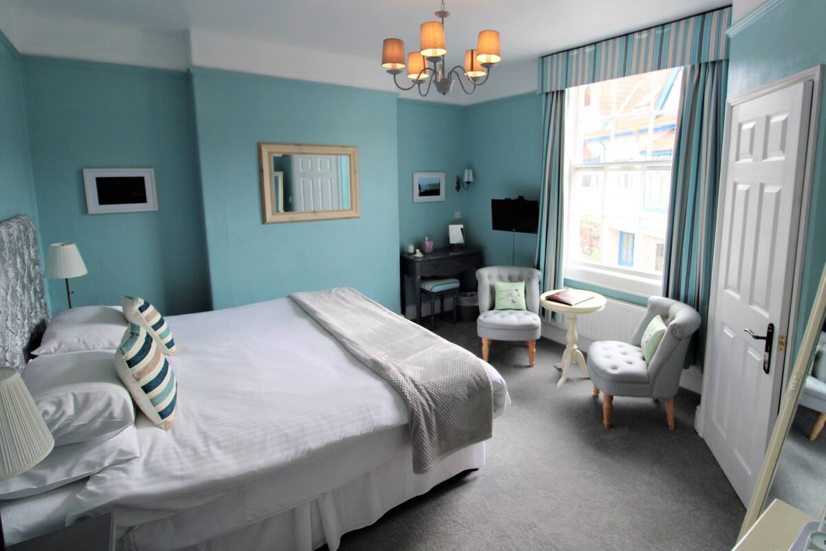A hotel room with a large bed, a desk, a chair, a television, and a window with curtains.