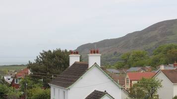 A residential area with houses featuring pitched roofs and chimneys, surrounded by greenery and hills in the background.