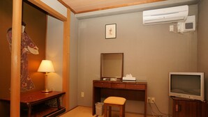 A hotel room with a wooden desk, a mirror, a television, and a wall-mounted air conditioner.