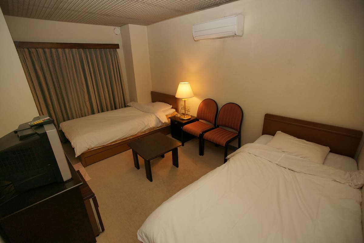 A hotel room with two beds, a desk with a TV, a lamp, and a chair.