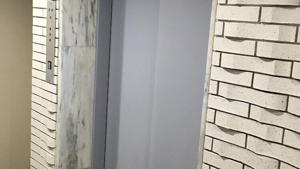 An elevator with a marble wall on one side and a brick wall on the other.
