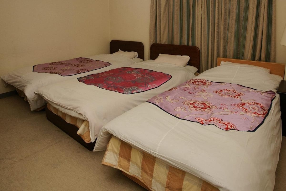 A room with two beds, a ceiling light, and a window with curtains.