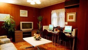 A room with a television, two computer monitors, a desk, a chair, a sofa, and a potted plant.