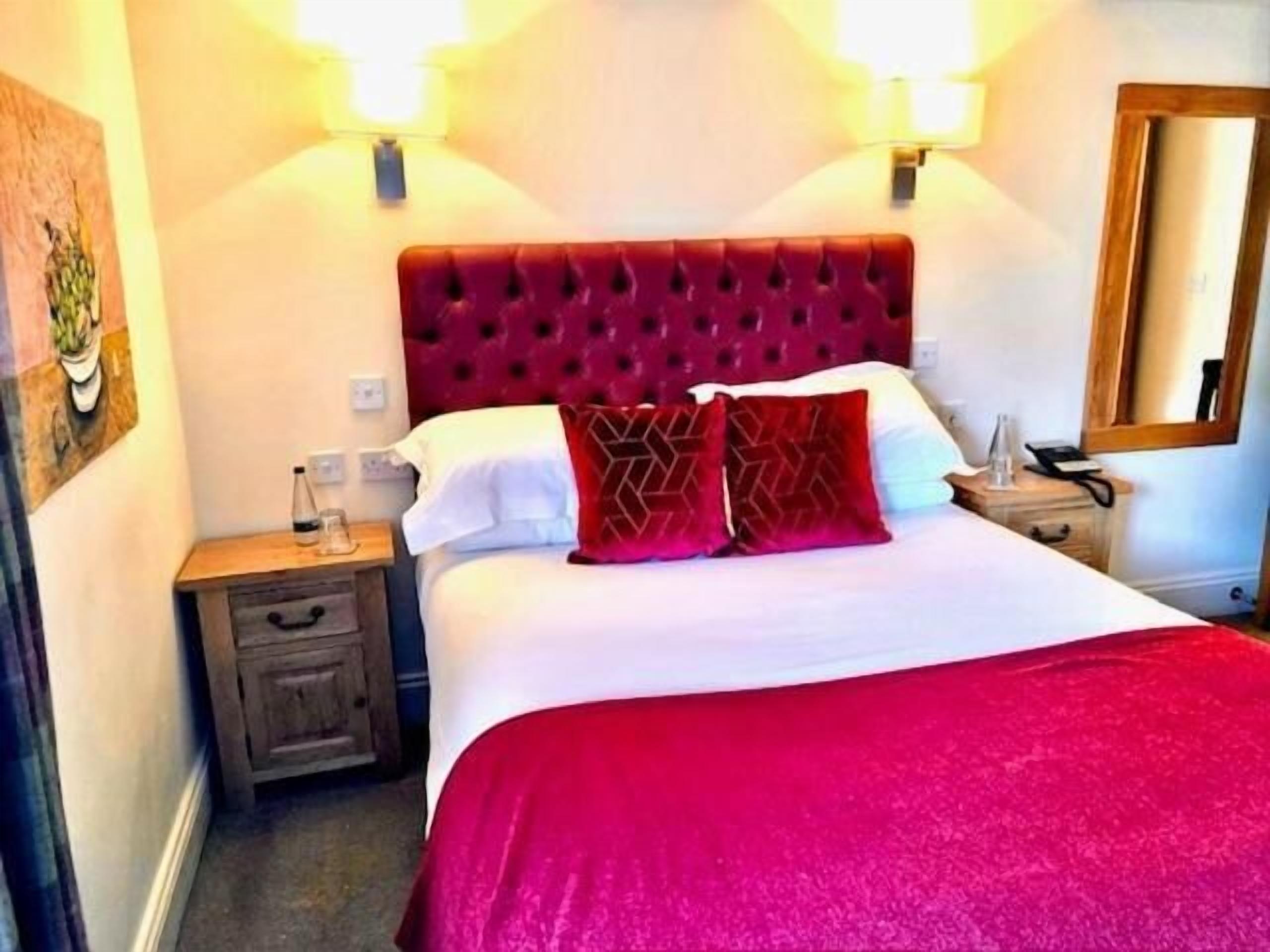 A hotel room with a large bed, a wooden nightstand, a bedside table, and a mirror.