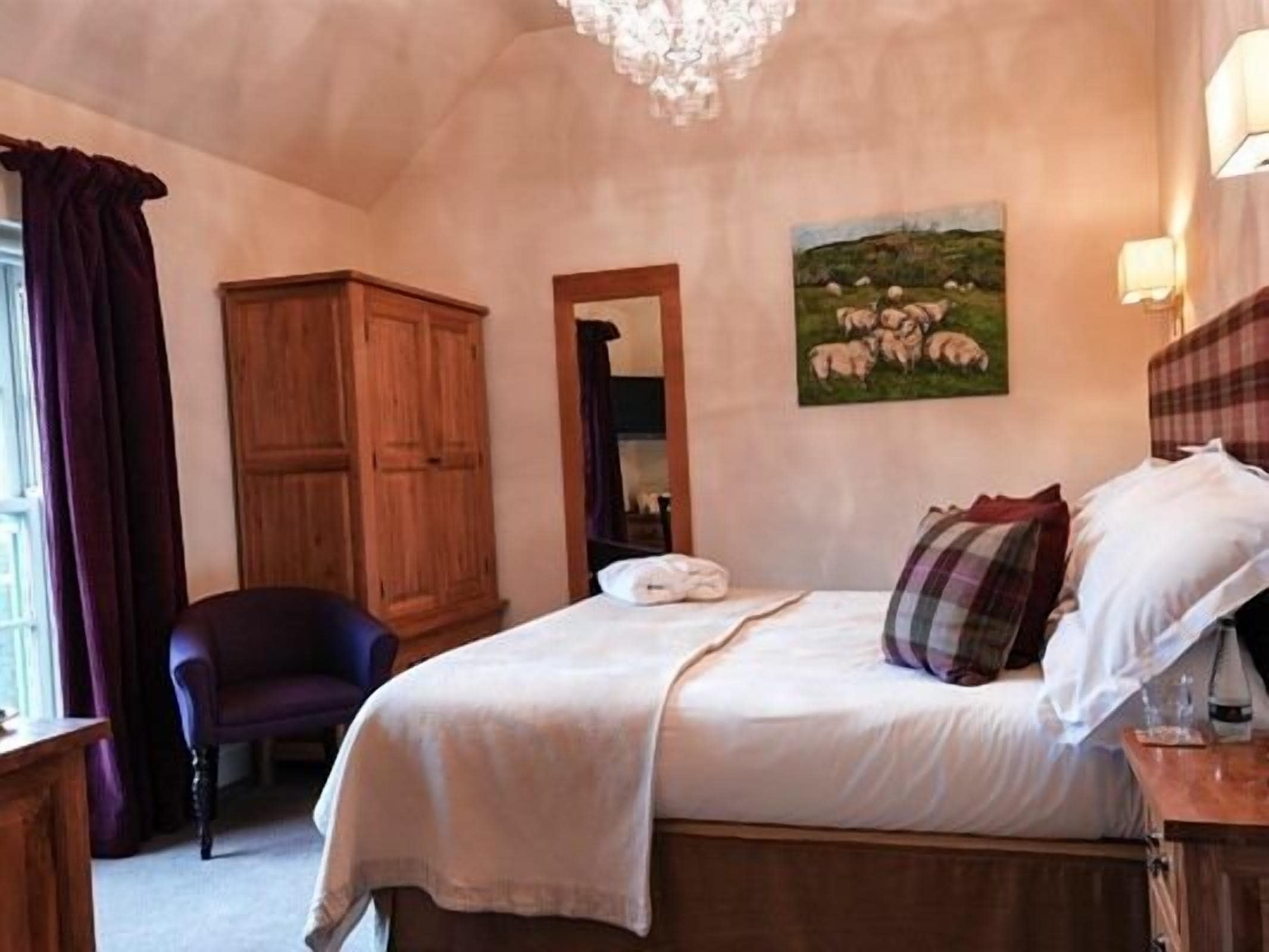 A bedroom with a bed, a wooden wardrobe, a chair, and a painting of sheep on the wall.