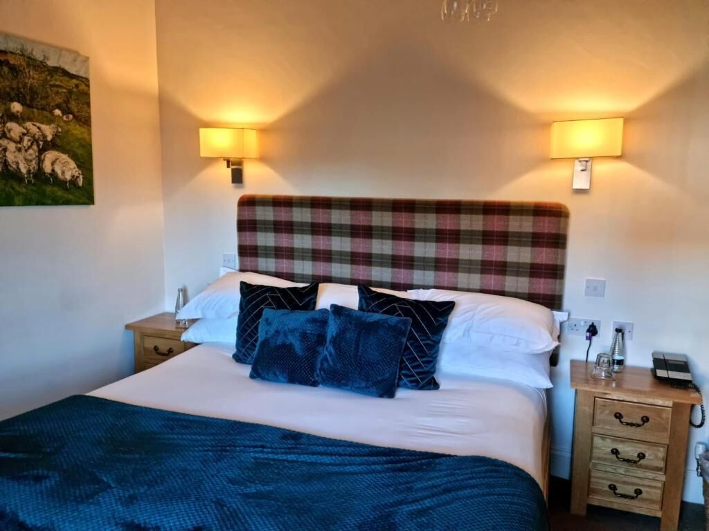 A bedroom with a plaid headboard, a bed with white and dark blue bedding, two bedside lamps, and a nightstand with a phone and a glass.