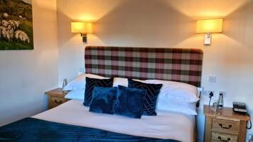A bedroom with a plaid headboard, a bed with white and dark blue bedding, two bedside lamps, and a nightstand with a phone and a glass.