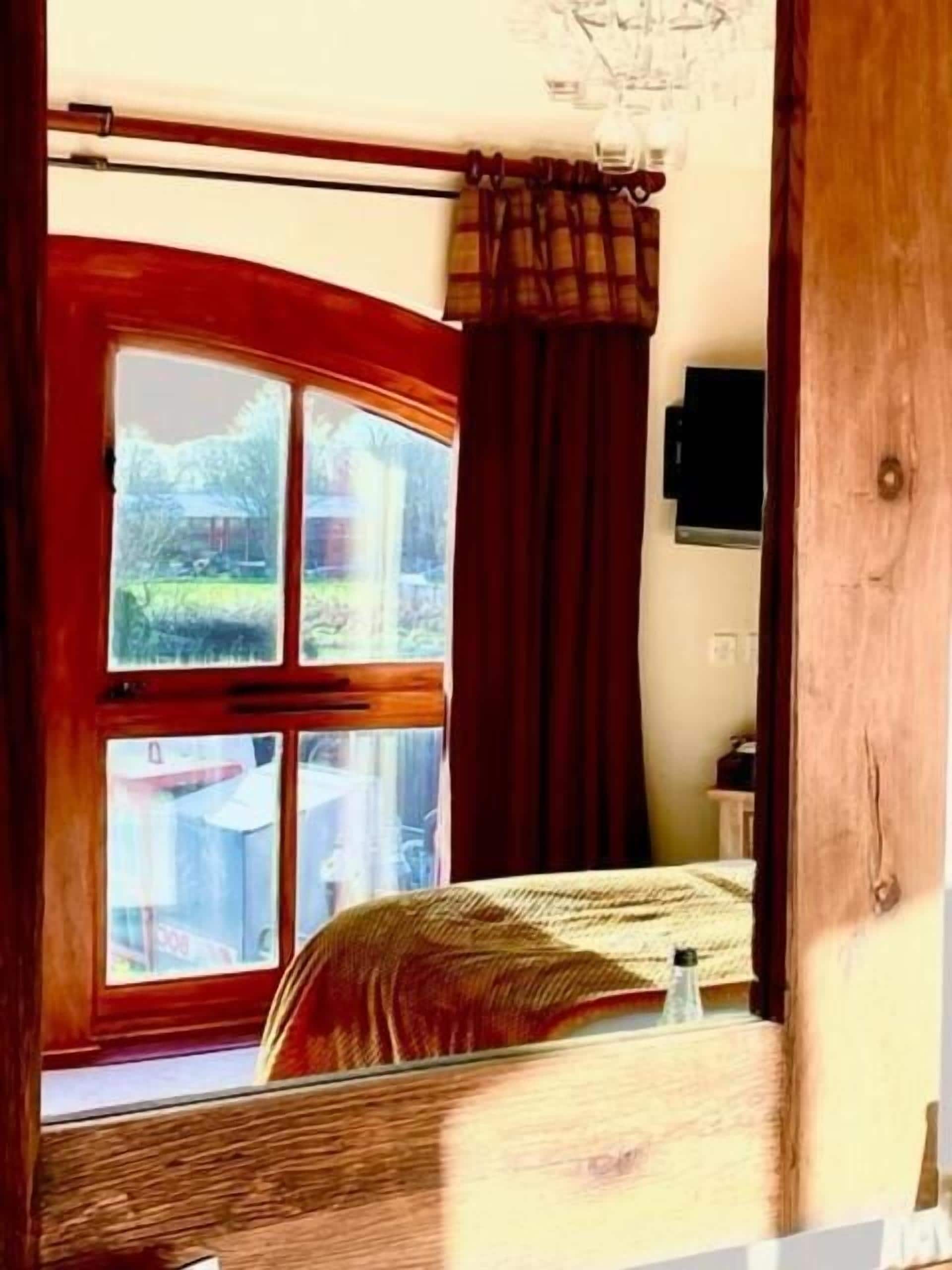 Una habitación con cama, ventana con cortinas, candelabro y televisor en la pared.