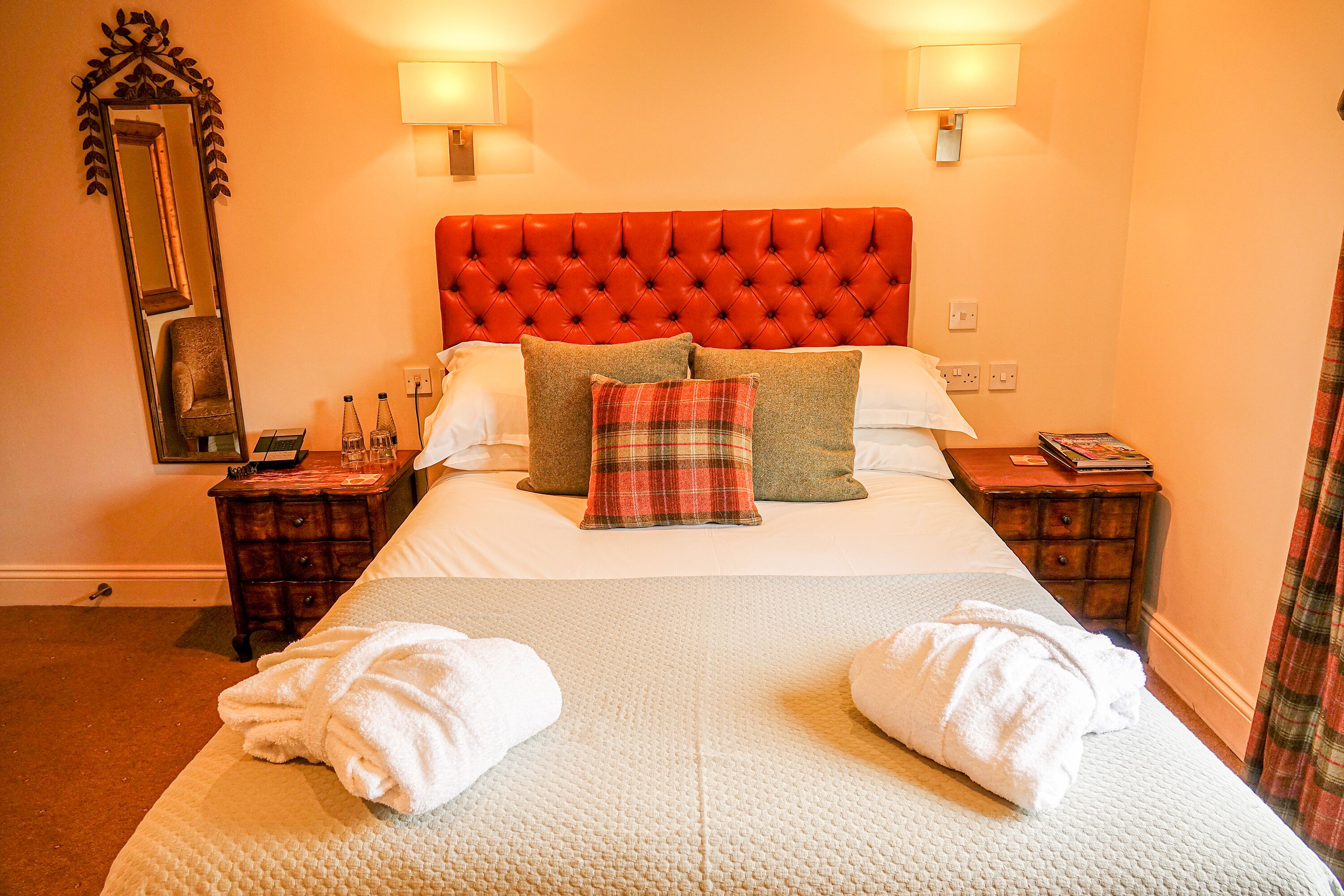 A hotel room with a large bed, two bedside tables, a mirror, and a red upholstered headboard.