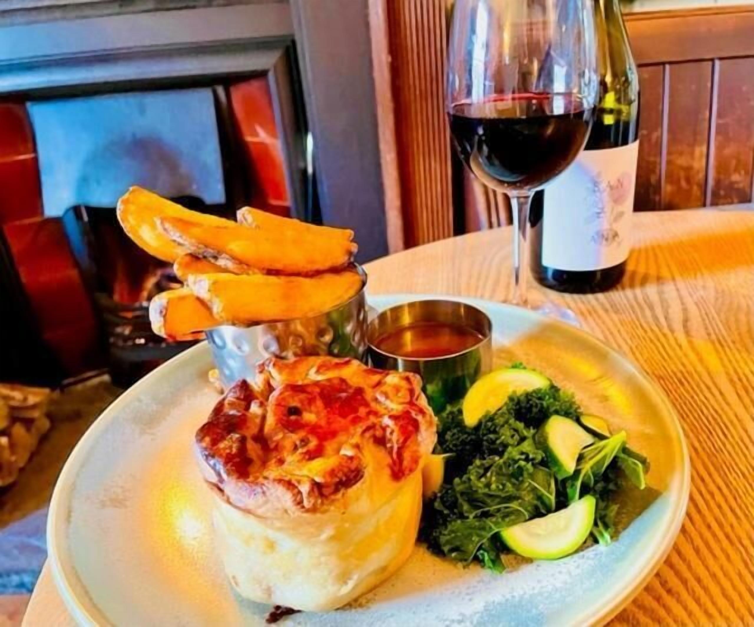 Un piatto con un sformato al forno, un bicchiere di vino rosso e una bottiglia di vino su un tavolo.