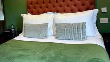 A hotel room with a green wall, a tufted brown headboard, white bedding, and two wall-mounted lamps.