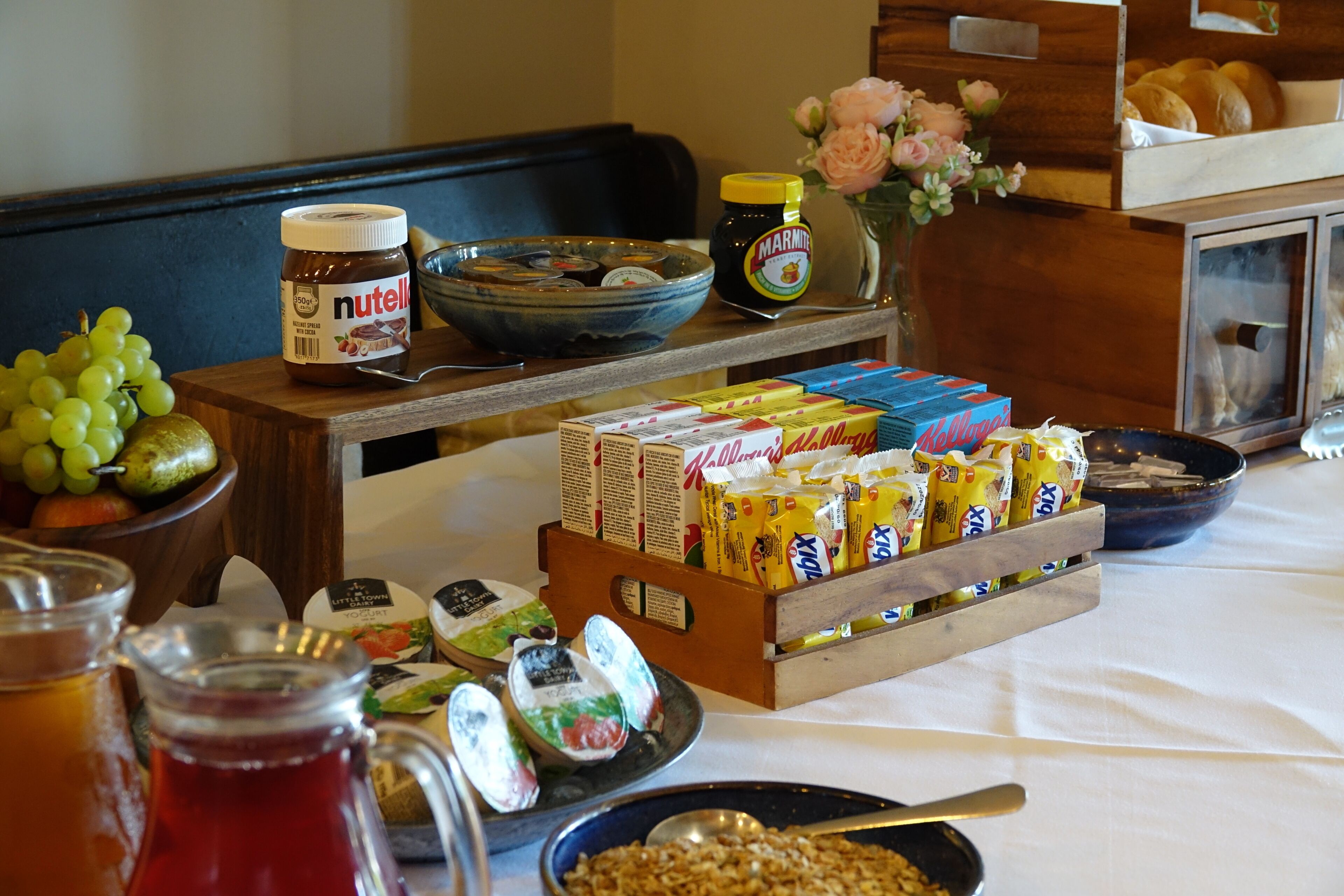 A breakfast buffet with various food items, including cereal boxes, jars of jam, and a bowl of fruit.