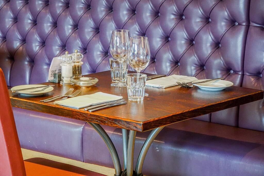 A dining table set with plates, glasses, and cutlery in a restaurant with a tufted leather booth seating.