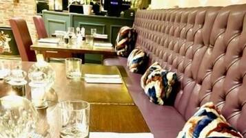 Un comedor con una mesa de madera dispuesta para dos personas, un banco tapizado en color púrpura y una zona de bar al fondo.