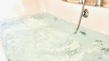 A bathtub with running water, a towel, and a candle on a table.