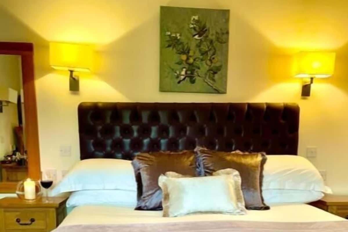 A hotel room with a large bed, two bedside lamps, a headboard, and a painting on the wall.