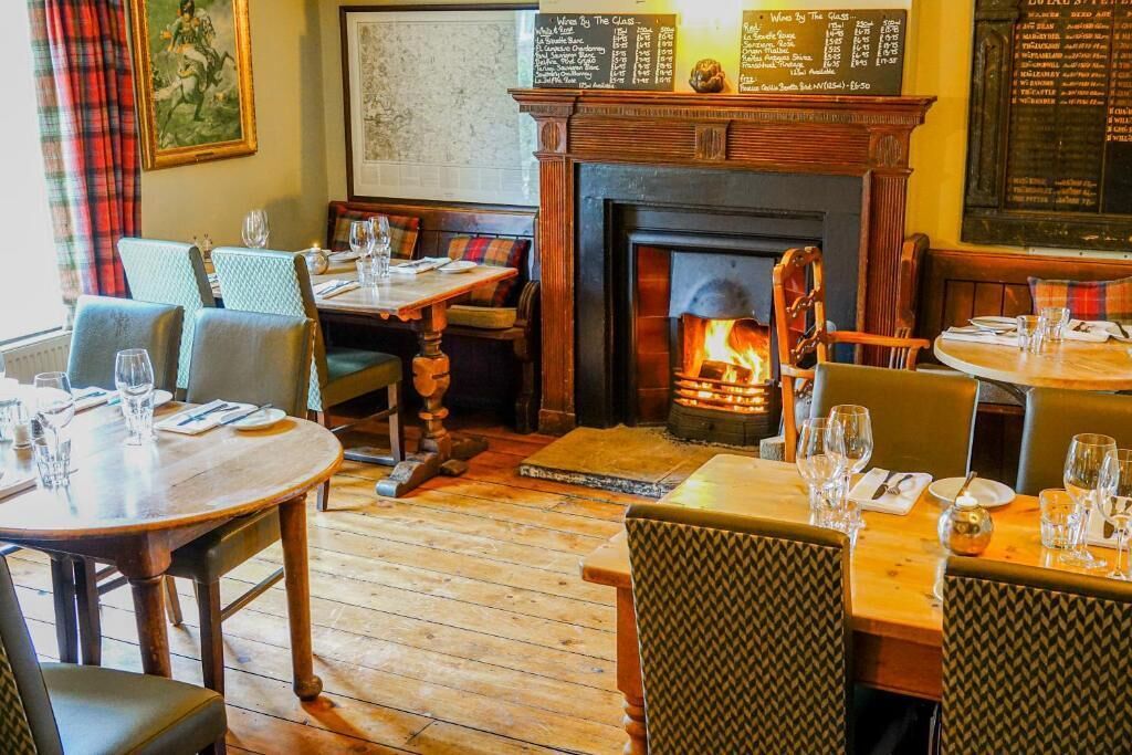 Un restaurante acogedor con suelo de madera, una chimenea y una pizarra con la carta.