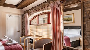 Une chambre confortable avec un mur en pierre, un lit doté d’une tête de lit miroir, un bureau avec une chaise et un radiateur.