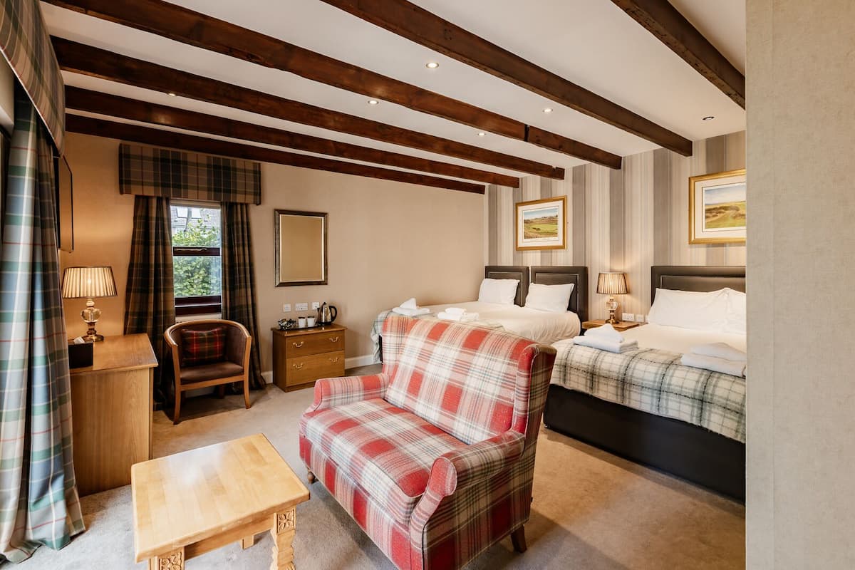Habitación de hotel con dos camas, un escritorio de madera, una silla, una mesita y una ventana con cortinas.