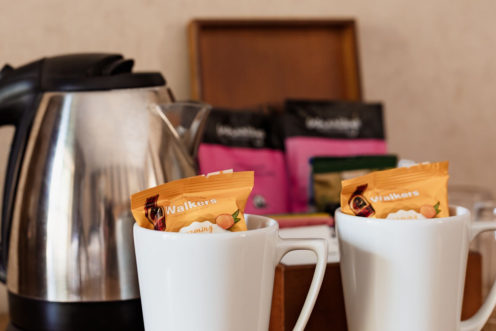 Two white mugs with packets of Walkers chewing gum. A silver electric kettle is in the background.