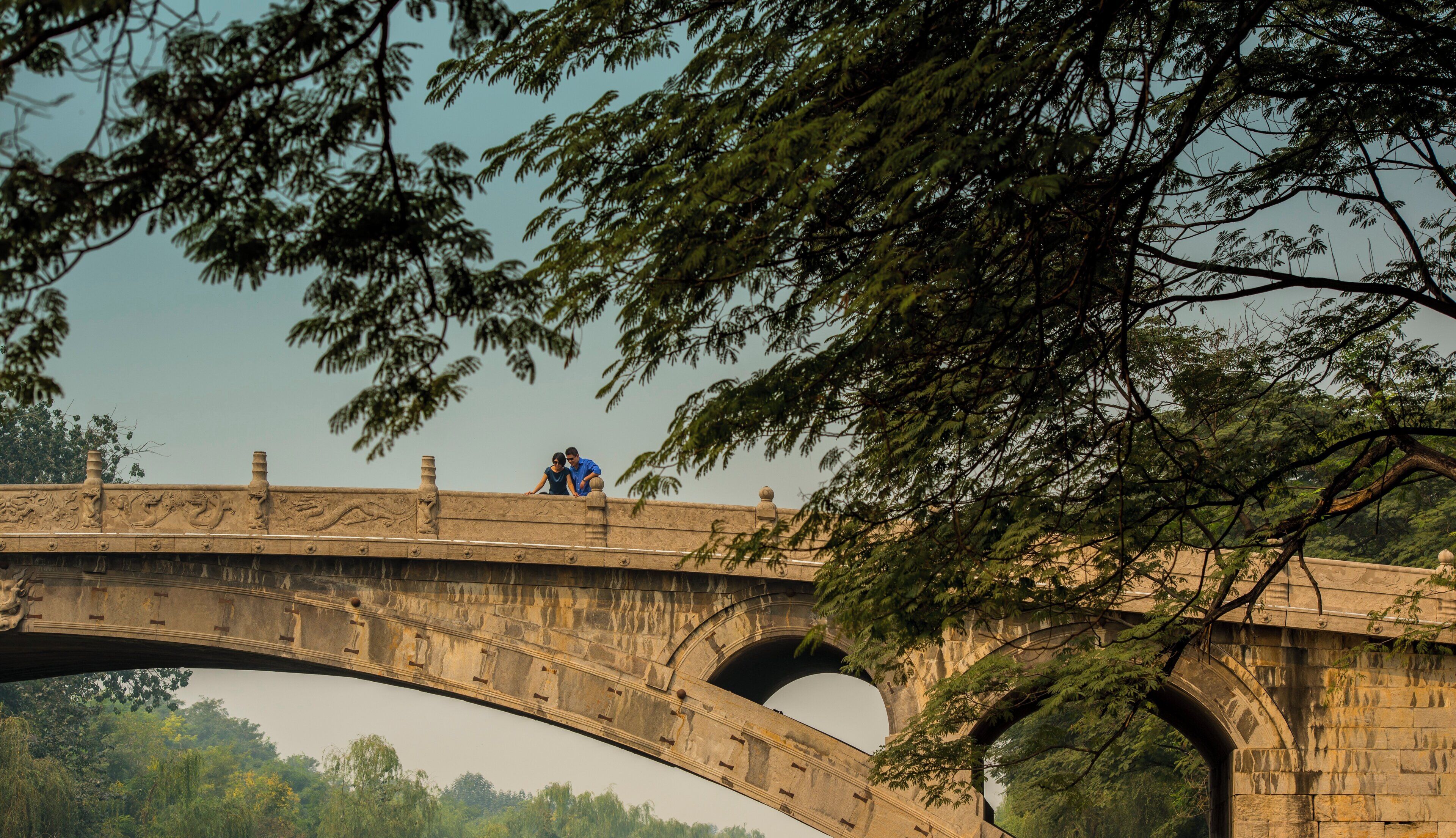 Un puente de piedra con esculturas ornamentales y dos personas sobre él.