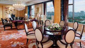 Amplia habitación de hotel con un comedor grande, asientos cómodos, una araña y vistas a la ciudad.