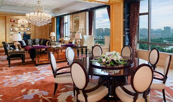 Amplia habitación de hotel con un comedor grande, asientos cómodos, una araña y vistas a la ciudad.