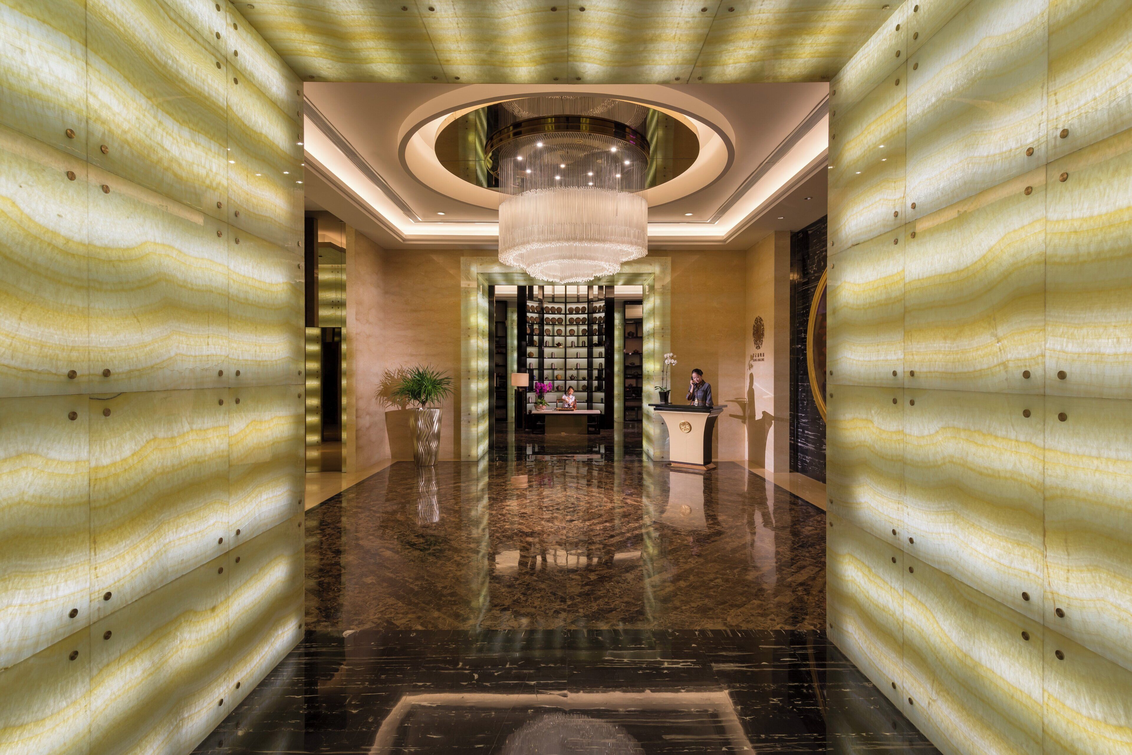 A lobby with a marble floor, a central chandelier, and a reception desk.