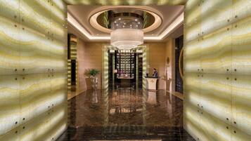 A lobby with a marble floor, a central chandelier, and a reception desk.