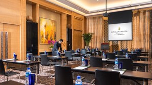 Una sala de conferencias con varias mesas y sillas, botellas de agua y una pantalla proyectora mostrando el nombre del hotel.