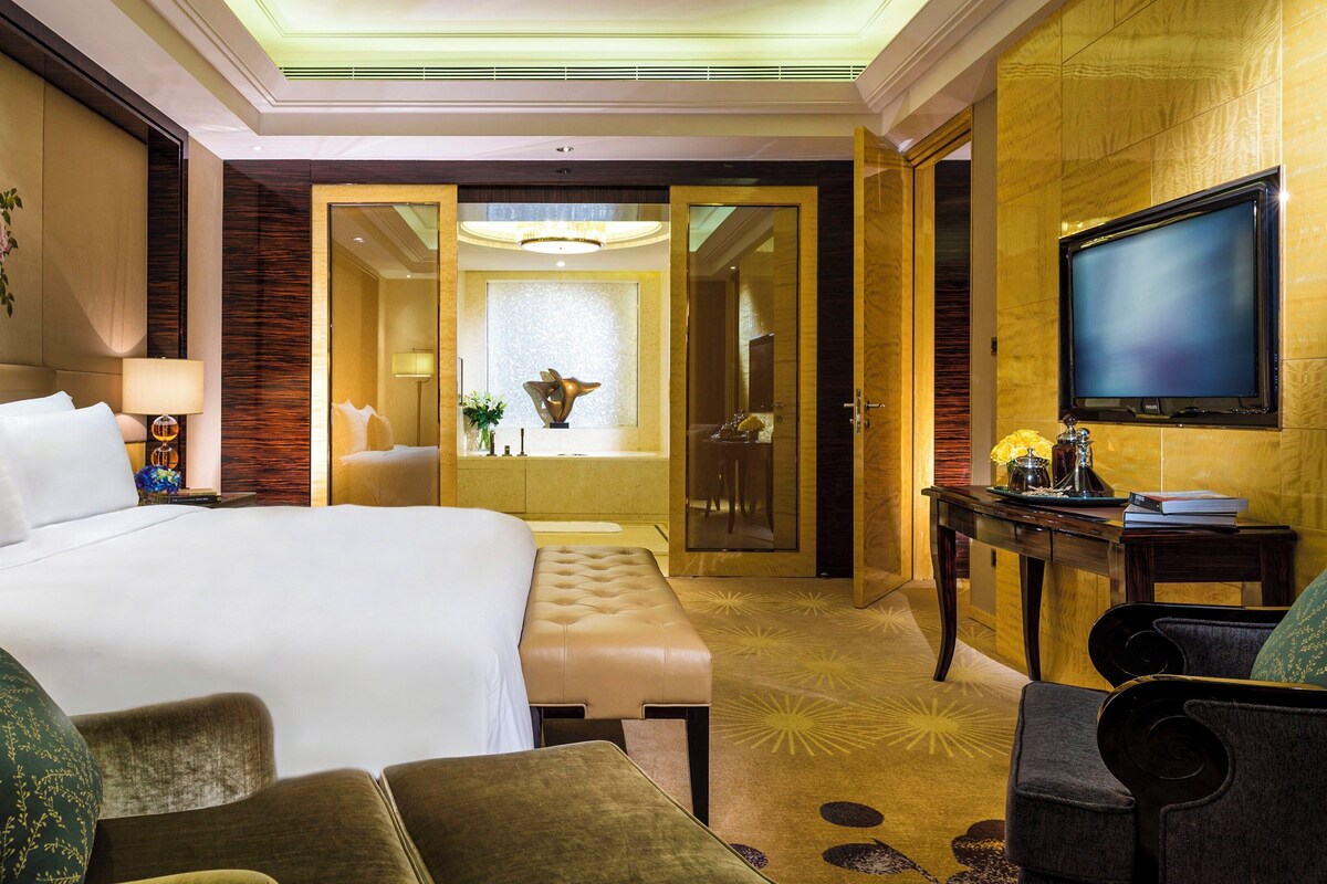 Hotelkamer met een groot bed, een zithoek met een tafel en stoelen, een televisie, en een badkamer zichtbaar door een geopende deur.