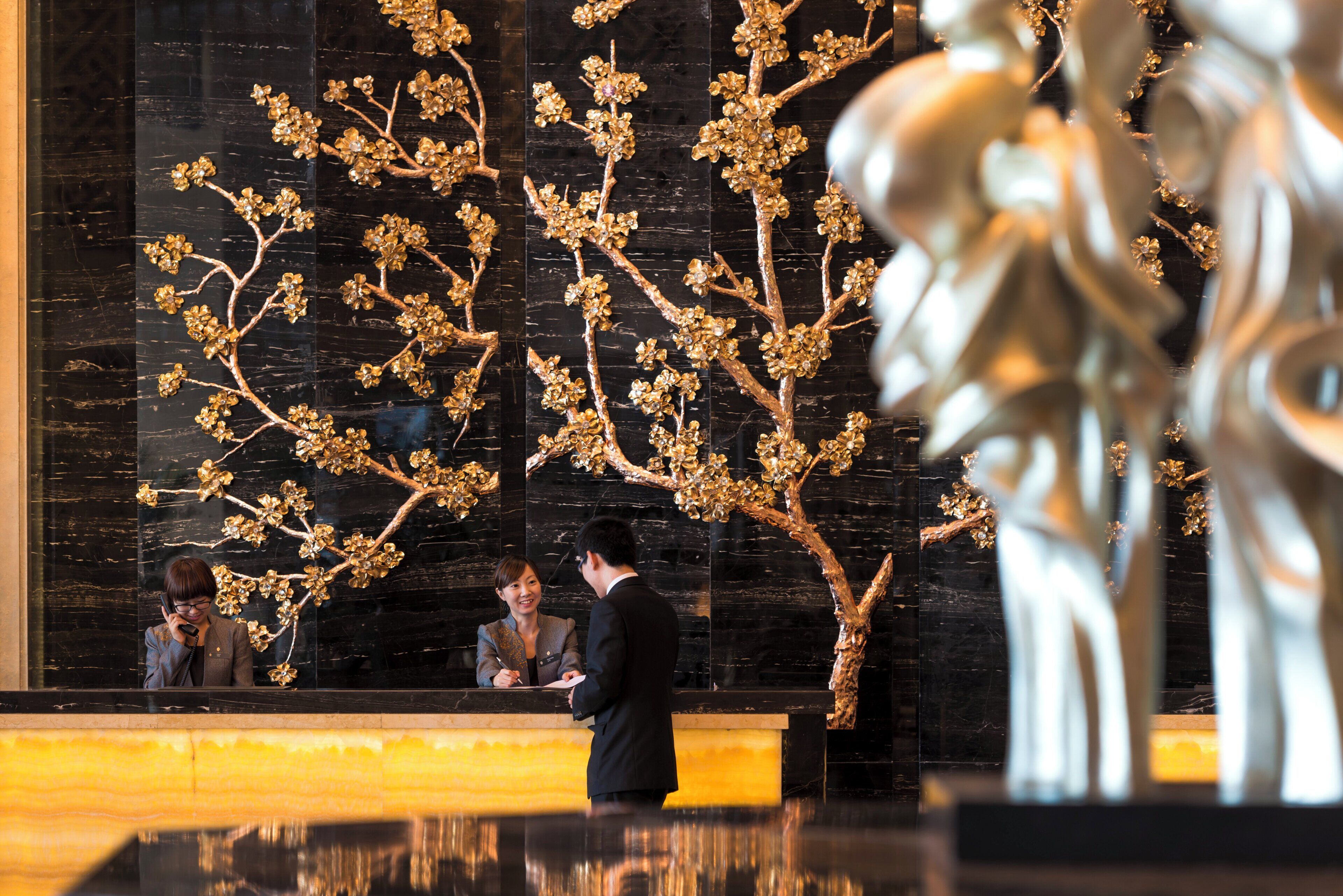A reception desk with a black marble wall and golden decorative elements.